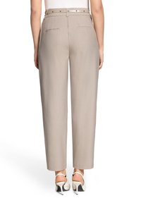 Pantalon beige taille haute avec une coupe ajustée, doté d'une ceinture avec une boucle en métal argenté et de deux poches arrière. Tissu lisse et texturé.