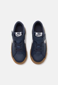 Baskets bleu marine avec une tige en cuir, des accents bleu clair et une semelle en caoutchouc marron. Elles sont dotées de lacets et d'une sangle Velcro pour un maintien sûr.