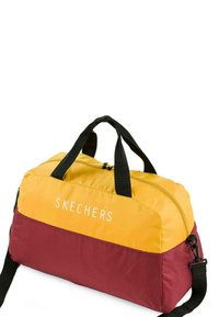 Bolsa de deporte Skechers en amarillo y burdeos, hecha de un tejido suave. Cuenta con un cierre de cremallera, asas negras y un logotipo destacado en el frontal.