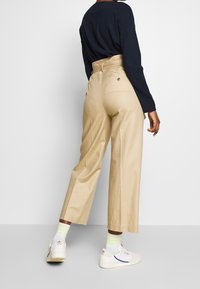 Beige Weitbein-Hosen mit hoher Taille und Gesäßtaschen, kombiniert mit einem schwarzen Langarmshirt und weißen Turnschuhen mit neonfarbigen Socken.