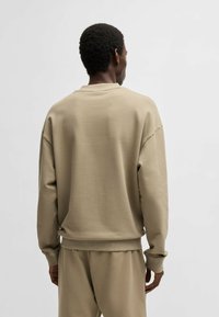 Felpa oversize beige con polsini e orlo a coste, dotata di colletto tondo e tessuto morbido e testurizzato. Design minimale senza loghi visibili.