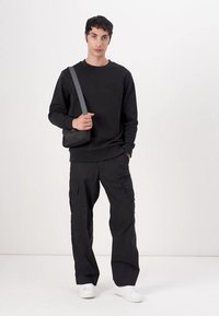 Schwarzer Pullover mit dezentem Logo, kombiniert mit schwarzen Cargo-Hosen mit mehreren Taschen und weißen Sneakers. Einfaches, lässiges Design.