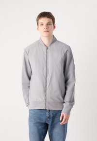 Jachetă bomber gri deschis, cu un front neted și mâneci texturate gri. Prezintă o închidere cu fermoar și manșete și tiv nervurat.