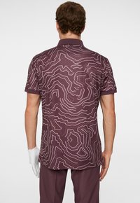 Kortärmad pikétröja i mörklila med ett konturlinjemönster i ljuslila. Slät textur och klassisk kragsdesign.