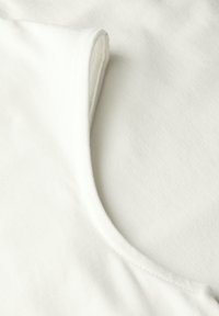 Tissu en coton blanc avec une texture lisse, présentant un col rond et des détails côtelés subtils sur les bords.