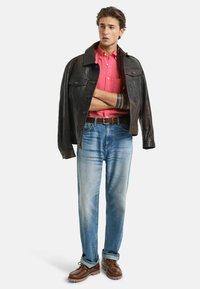 Lederjacke, rosa Hemd mit Knöpfen, hellblaue Jeans, braune Schnürschuhe und ein brauner Gürtel; lässiges Outfit mit kontrastierenden Farben.