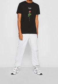 Černé bavlněné tričko s grafickým motivem červené růže a bílým textem "ztracená mládež" nad ní. Nosit s bílými kalhotami a teniskami.