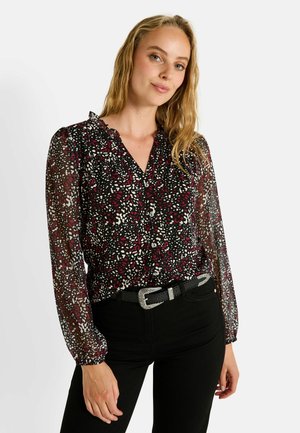 Blouse noire avec des motifs abstraits éclatants en rouge, blanc et rose ; manches longues en voile ; fermeture à boutons sur le devant ; col volanté ; associée à un pantalon noir.