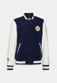 Marineblauwe varsityjack met witte leren mouwen, ribbelmanchetten en kraag; heeft een logo-patch en twee voorkanten zakken.