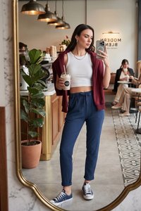 Ung kvinde i afslappet tøj, der holder en iskold drik, tager spejlselfie inde i en moderne café med kunder siddende i baggrunden.