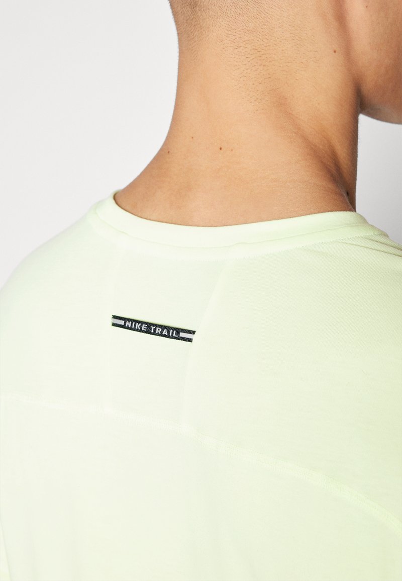 T-shirt Nike Trail vert clair avec col rond, manches courtes et un logo noir et blanc brodé à l'arrière près du cou.