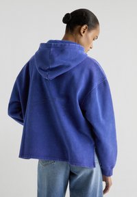 Paarse hoodie met een relaxte pasvorm, voorzien van een doodskop- en kruisbottenontwerp in rhinestones op de achterkant, gemaakt van zachte katoen.