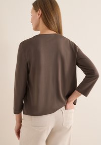 Haut marron à manches longues avec une texture lisse et une coupe décontractée, associé à un pantalon beige clair avec poches arrière.