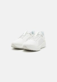 Hvide atletiske sneakers med en tekstureret overdel af stof, polstret krave og lyse snørebånd. Sålens yderside har et robust mønster for bedre greb.