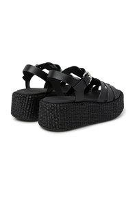 Sandali platform neri con suola tessurizzata intrecciata, dotati di ampie cinghie incrociate e un accento con fibbia laterale. Realizzati in materiale sintetico.