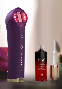 Purple handheld device with red LED lights, rounded top, control buttons, and a gold accent. Includes a red and black serum bottle beside it.