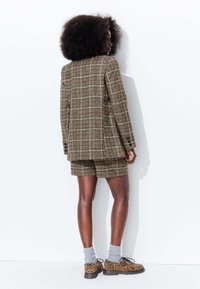 Ensemble blazer et shorts à carreaux bruns, avec un tissu texturé et deux boutons sur le blazer. Assorti avec des chaussettes grises et des chaussures à imprimé léopard.