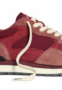 Zapatilla de ante en color burdeos y rosa con cordones blancos, suela de goma y un cordón desatado colgando suelto sobre un fondo blanco.