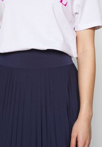 Marinblå plisserad kjol med ett texturerat tyg och en åtsittande midja, i kombination med en ljusrosa T-shirt med fet fuchsia-text.