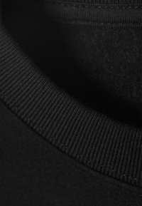 Col de sweat-shirt en coton noir montrant une texture côtelée et un intérieur doux. Gros plan mettant en évidence le tissu lisse et les détails de couture nets.