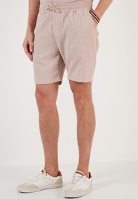 Lichtroze, gestructureerde shorts met een elastische tailleband en trekkoord, voorzien van zijzakken en een losse pasvorm. Gepaard met witte sneakers.