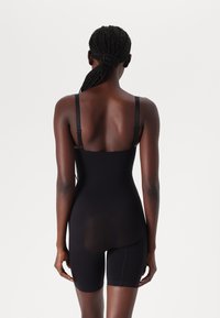 Svart bodysuit med tunna justerbara band, knä-lång, tillverkad av mjukt, stretchigt material, med en genomskinlig bakpanel och detaljerad sömnad.