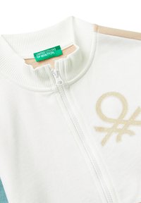 Giacca bianca con zip, colletto a costine, blocchi di colore beige e teal, e logo glitterato beige dei United Colors of Benetton sul petto.