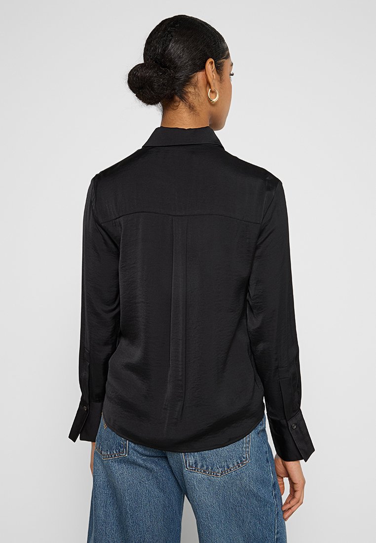 Zwarte longsleeve shirt met een gladde textuur, puntige kraag, achterste schoudernaad en knopenmanchetten, gecombineerd met blauwe recht afgesneden jeans.