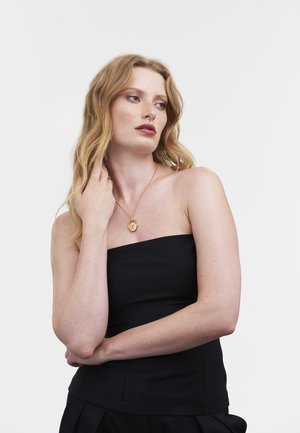 Black strapless top with a fitted design. Golden pendant necklace with a round, intricate detail. Wavy, medium-length hair.