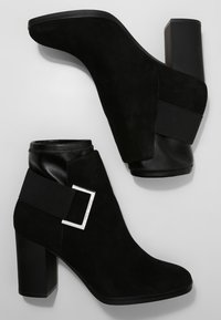 Stivaletti alla caviglia in suede nero con una larga fascia e fibbia quadrata in argento, punta arrotondata e tacco spesso con una finitura nera liscia.