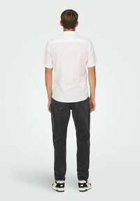 Camisa blanca de manga corta, textura suave, con cuello abotonado, pantalones vaqueros negros, color oscuro, diseño sencillo y zapatillas en blanco y negro.