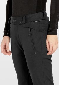 Zwarte broek van een textuurstof, met zijzakken met rits en een tailleband met knoopsluiting. Logo zichtbaar op de linker bovenbeen.
