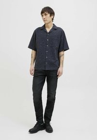 Rövidujjú, virágmintás sötét ing, gombos designnal, bal oldali zsebbel, fekete farmernadrággal és fekete cipővel párosítva.