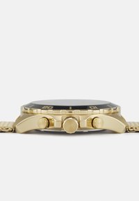 Montre-bracelet dorée avec une lunette noire, un cadran texturé, et trois poussoirs sur le côté. Elle dispose d'un bracelet en métal avec un design de maillons.