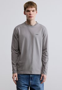 Γκρι μακρυμάνικο T-shirt με στρογγυλή λαιμόκοψη και μικρό μαύρο λογότυπο "BOSS" στο στήθος, σε συνδυασμό με μπλε τζιν παντελόνι.