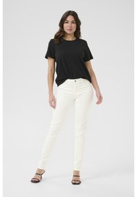 Un t-shirt noir à manches courtes associé à un jean skinny blanc. La tenue est complétée par des sandales noires à brides. Tissu lisse et design ajusté.