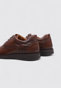 Zapatos de cuero marrón con puntera redonda, textura suave y diseño de cordones. Suela de goma negra gruesa con un sutil detalle de costura en los laterales.