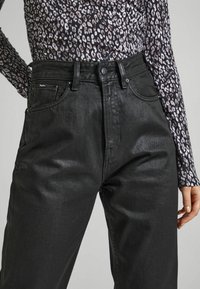 Jeans de mezclilla negra con un corte clásico, que cuentan con cinco bolsillos, pasadores para cinturón y un cierre de botón, combinados con una blusa de manga larga estampada.