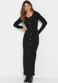 Robe maxi noire à côtes avec manches longues, encolure ronde, détails de boutons dorés et ceinture nouée à la taille. Tissu texturé, design ajusté.