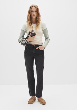 Jeans neri a gamba dritta con vita alta, abbinati a una camicia a maniche lunghe crema e grigia e scarpe in stile mocassino color beige.