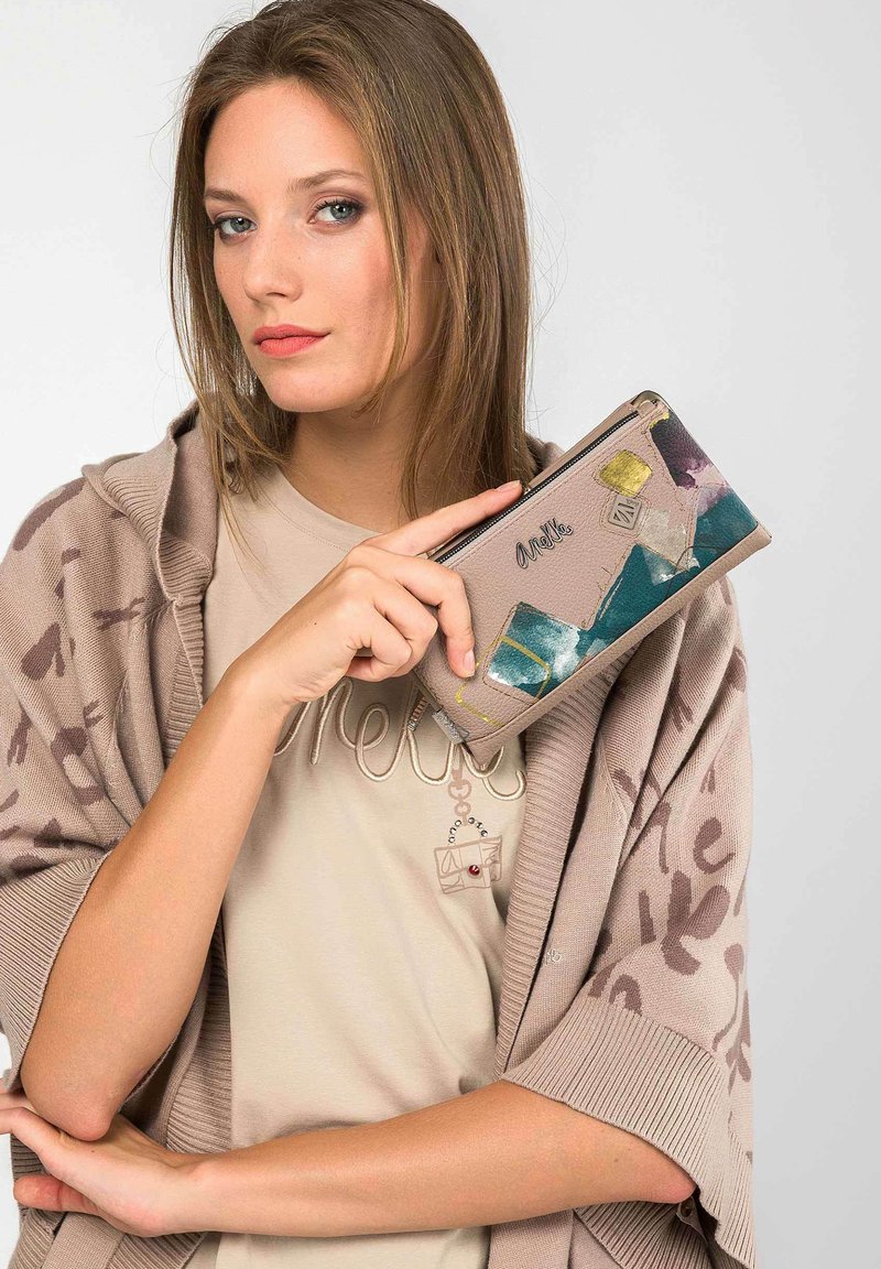 Cartera colorida en tonos apagados, con patrones geométricos y detalles en relieve. Textura suave con cierre de cremallera y elementos de acento.