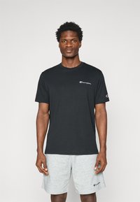 Schwarzes Baumwoll-T-Shirt mit Rundhalsausschnitt und kurzen Ärmeln, mit einem weißen Champion-Logo auf der Brust und einem grauen Logo am Ärmel.