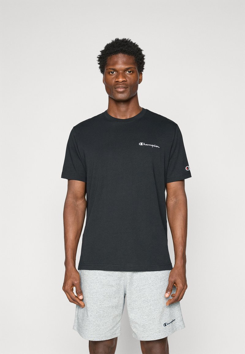 Schwarzes Baumwoll-T-Shirt mit Rundhalsausschnitt und kurzen Ärmeln, mit einem weißen Champion-Logo auf der Brust und einem grauen Logo am Ärmel.
