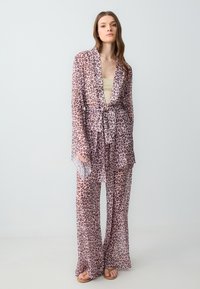 Ensemble d'extérieur à motif léopard en tissu transparent, avec un design à enroulement, des manches longues et un pantalon ample assorti avec une taille ceinturée.