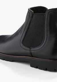 Botte Chelsea en cuir noir avec un panneau élastique texturé, une silhouette incurvée et une semelle en caoutchouc robuste. Fini lisse agrémenté de coutures.