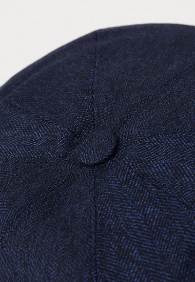 Căciulă de tip newsboy din lână de culoare albastru închis, cu un model texturat de herringbone și un buton acoperit cu țesătură în partea de sus.