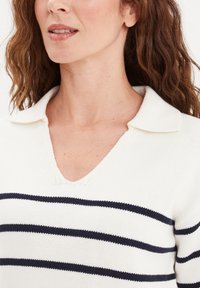 Maglione bianco con strisce orizzontali blu navy, scollo a V e colletto ripiegato. Il tessuto sembra morbido, lavorato a maglia e con una finitura testurizzata.