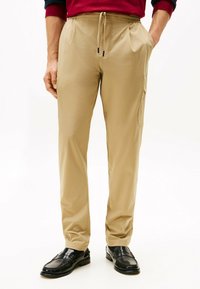 Pantalones ligeros beige con una cintura elástica y cordón, con bolsillos laterales y un corte relajado, combinados con mocasines negros.
