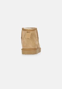 Stivaletto alla caviglia in suede beige con rivestimento soffice, punta rotonda, dettagli cuciti e suola in gomma piatta. Il retro presenta una piccola linguetta per una facile calzata.