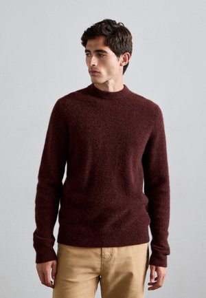 Burgundy knit sweater with a high neckline, soft texture, and long sleeves, paired with light khaki pants. Simple, fitted design.